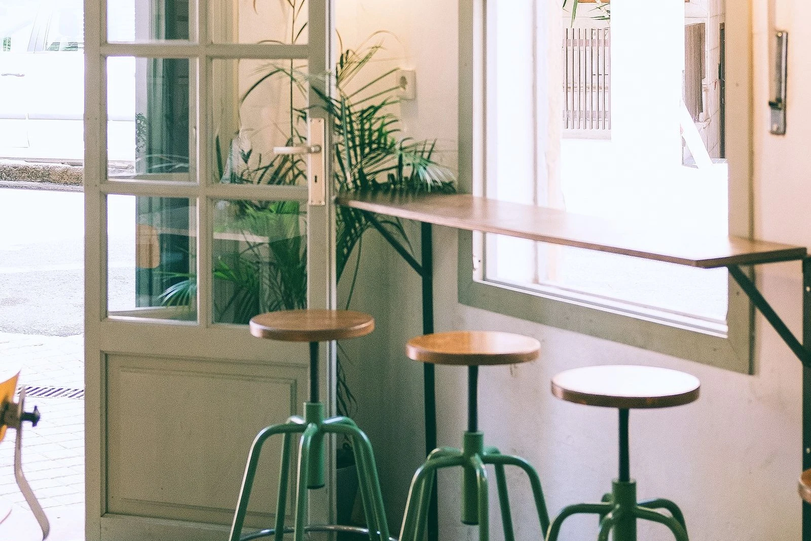 カフェの入り口に置かれた木製スツールと観葉植物のイメージ